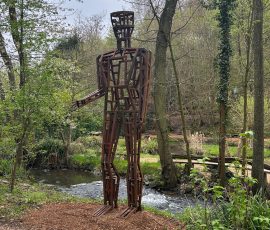 Große eiserne Metallskulptur Antropo Metron von Künstler Heinze in der Natur an einem Bachlauf.