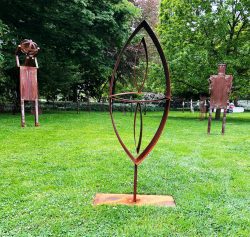 Abstrakte, linsenförmige Rahmenskulptur aus rostpatiniertem Stahl im Vordergrund einer Parkwiese mit weiteren Skulpturen.
