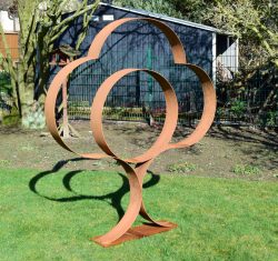 Abstrakte Außenskulptur aus breit geschwungenen Stahlbändern mit Rost-Patina, platziert auf einem Rasen mit ausgeprägtem Schattenwurf.