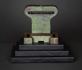 Symmetrische, abstrakte Skulptur aus einem grünlich patinierten Gusseisen-Element auf einem mehrstufigen, schwarzen Sockel.