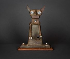Kompakte, abstrakte Assemblage-Skulptur aus rostfarbenem Metall mit zwei markanten Spitzen und augenähnlichen Elementen auf Holzsockel.