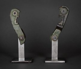 Duo aus zwei spiegelbildlich angeordneten, mechanisch anmutenden Metallobjekten mit Gelenkstrukturen auf hellen Sockeln.