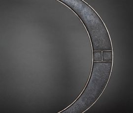 Abstrakte Nahaufnahme eines präzise gearbeiteten, dunklen Metallbogens mit geometrischen Aussparungen und Segmentierungen.
