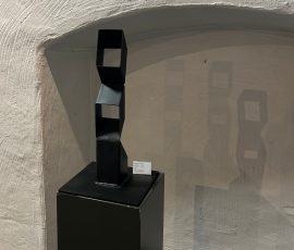Abstrakte, geometrische Skulptur aus matt schwarzem Stahl, zusammengesetzt aus kantigen, kubischen Elementen auf einer dunklen Stele.