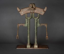 Abstrakte, anthropomorphe Assemblage-Skulptur aus patiniertem Metall und Holz mit breitem, ornamentalem Kopfelement und filigranen Gliedmaßen.